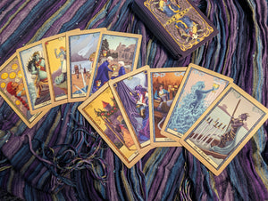Ten tarot cards lay in two fans of five cards, with the rest of the cards stacked above it, on a striped scarf.